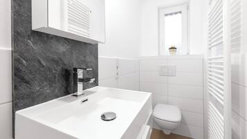 Ein modernes Badezimmer mit einem weißen Waschbecken, einer Toilette und einem Fenster mit Blick.
