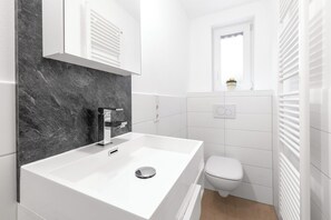 A modern bathroom with a white sink, a toilet, and a window with a view.