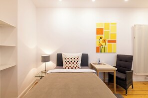A bedroom with a bed, a desk, a chair, a lamp, and a wall art piece.
