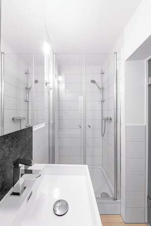 A modern bathroom with a white sink, a glass shower enclosure, and a marble accent wall. - Single apartment with kitchenette and terrace, central location (Bad Ems)