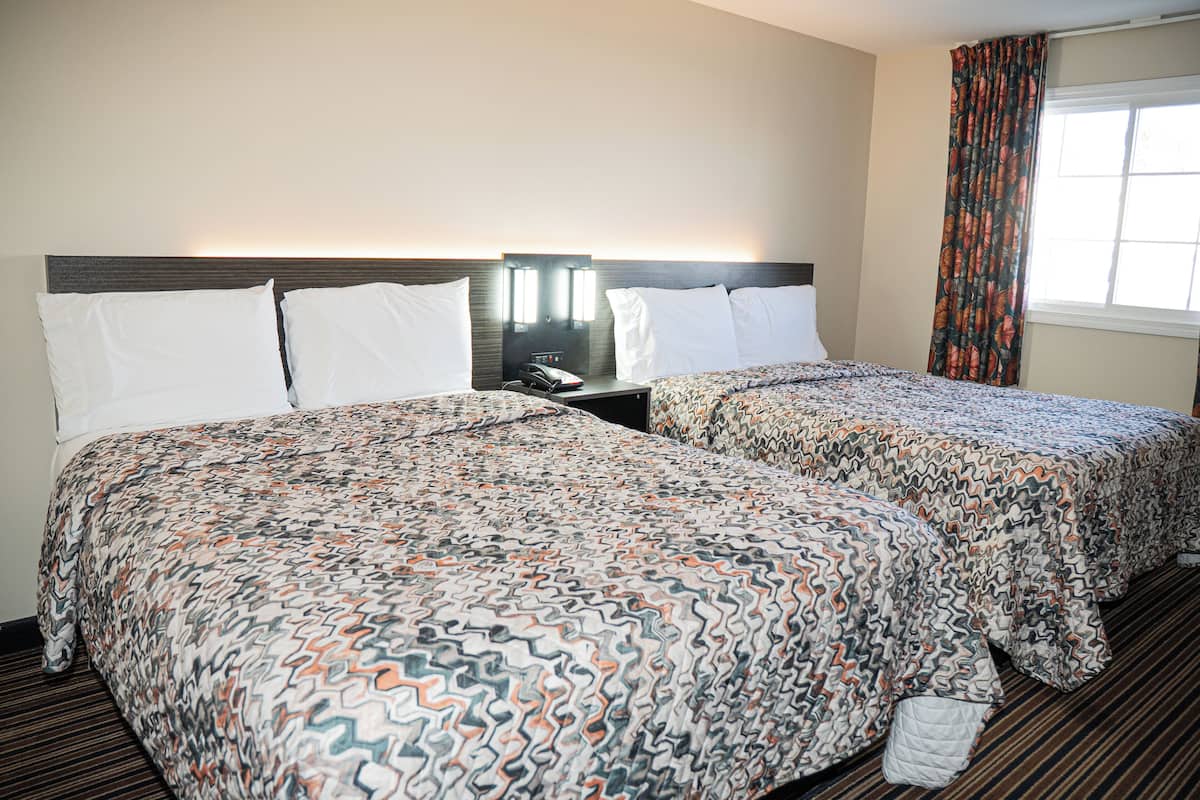 A hotel room with two beds, a nightstand with a phone, and a window with curtains.