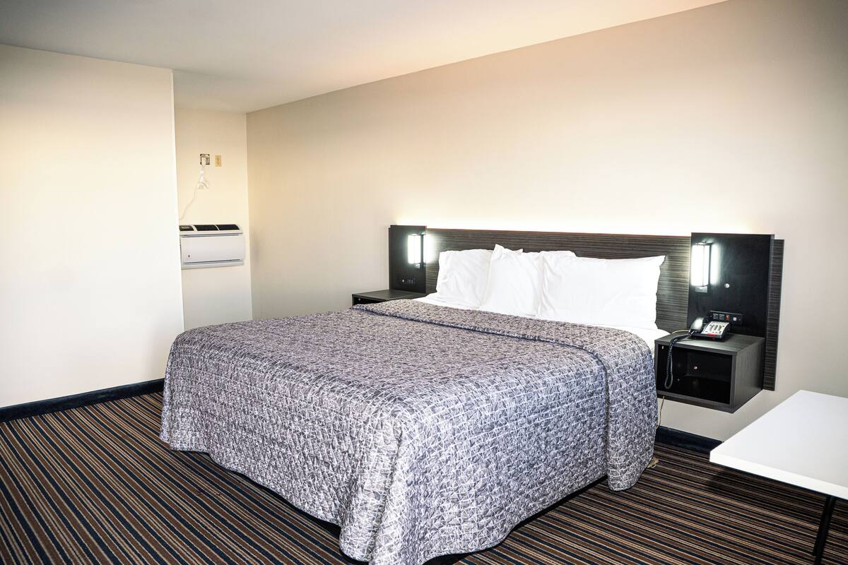 A hotel room with a large bed, a bedside table with a phone, and a wall-mounted air conditioning unit.