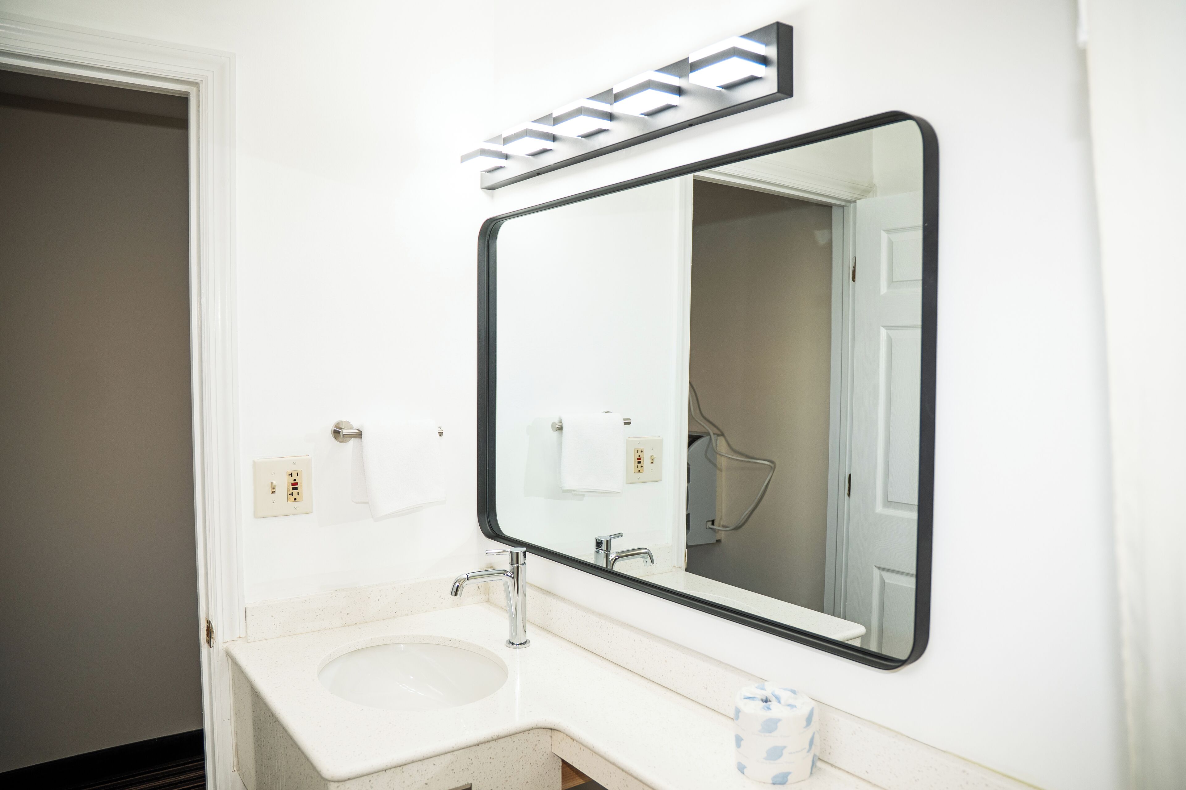 A bathroom with a white sink, a large mirror, and a towel dispenser.