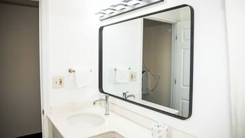 A bathroom with a white sink, a large mirror, and a towel dispenser.