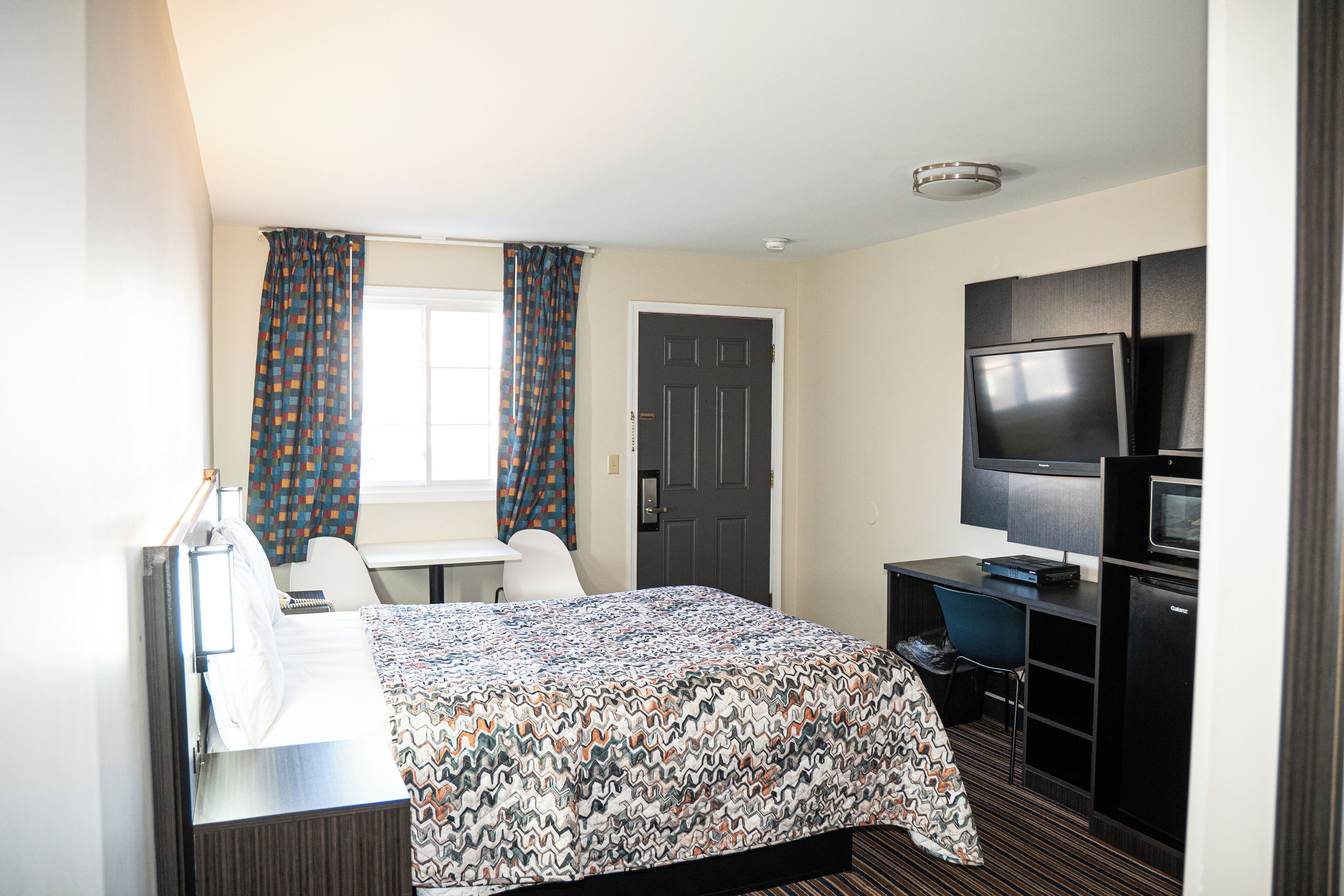 A hotel room with a bed, desk, chair, television, and a door.