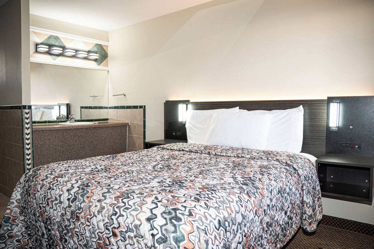 A hotel room with a large bed, a nightstand, a mirror, and a bathroom with a sink and towel rack.