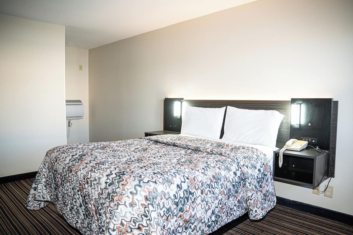 A hotel room with a large bed, a bedside table with a phone, and a wall-mounted light.