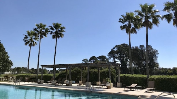 A pool area with lounge chairs and a pergola, surrounded by palm trees. - Peninsula Links B102 (Gulf Shores)
