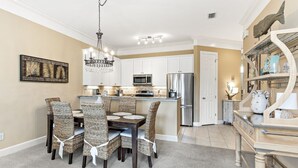 A modern kitchen with white cabinets, a stainless steel refrigerator, and a dining area with wicker chairs. - Peninsula Links B102 (Gulf Shores)