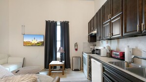 A compact living space with a kitchenette, a dining area, and a view of a building through a window. - Chic and Roomy Urban Getaway in New Orleans (New Orleans)