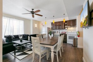 Une cuisine moderne avec un coin repas, un ventilateur de plafond et une grande fenêtre agrémentée de rideaux légers.