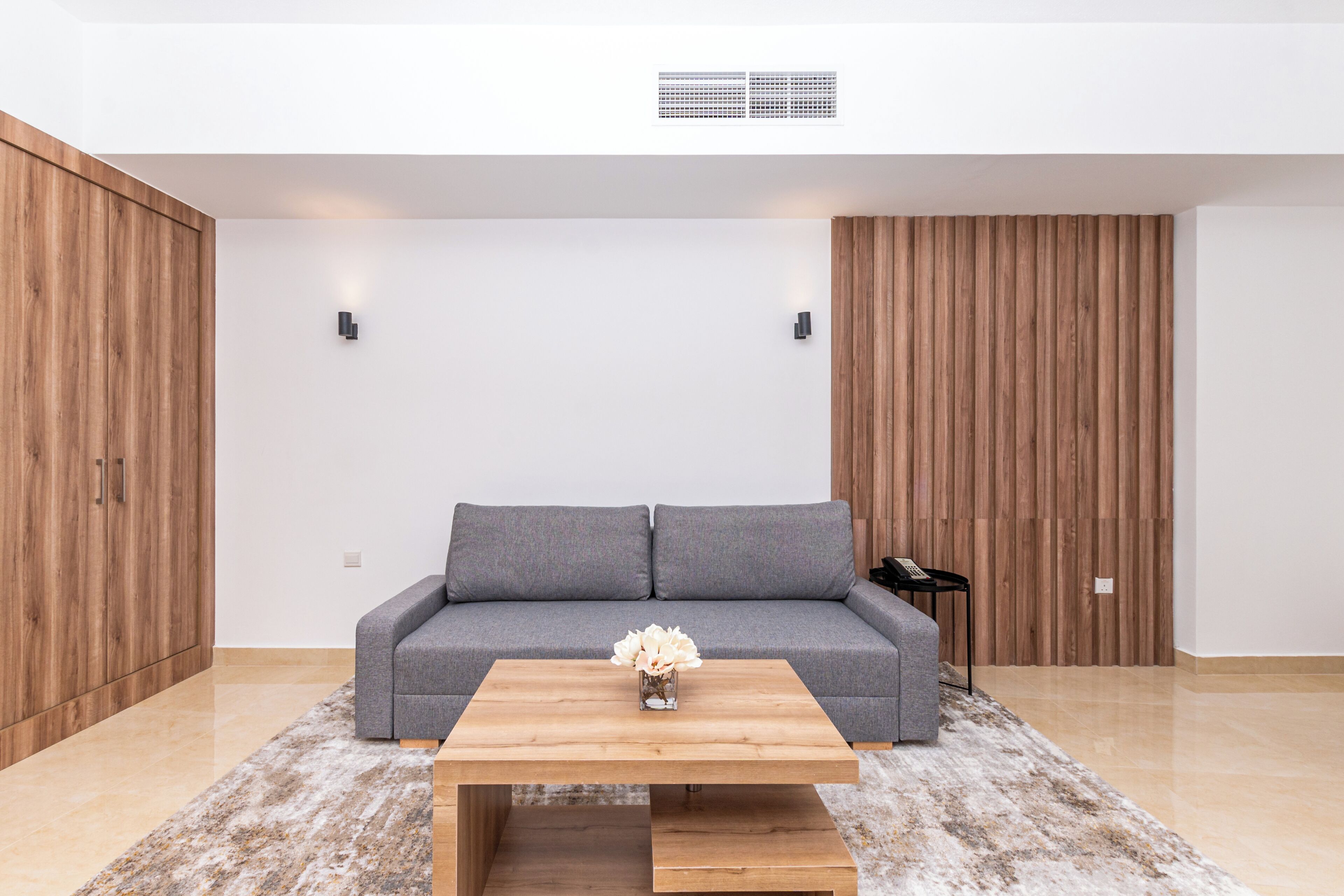 Een moderne woonkamer met een grijze bank, een houten bijzettafeltje en een kleine vaas met bloemen.
