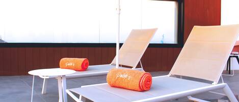 Two sun loungers with towels, a table, and an umbrella on a balcony with a view.