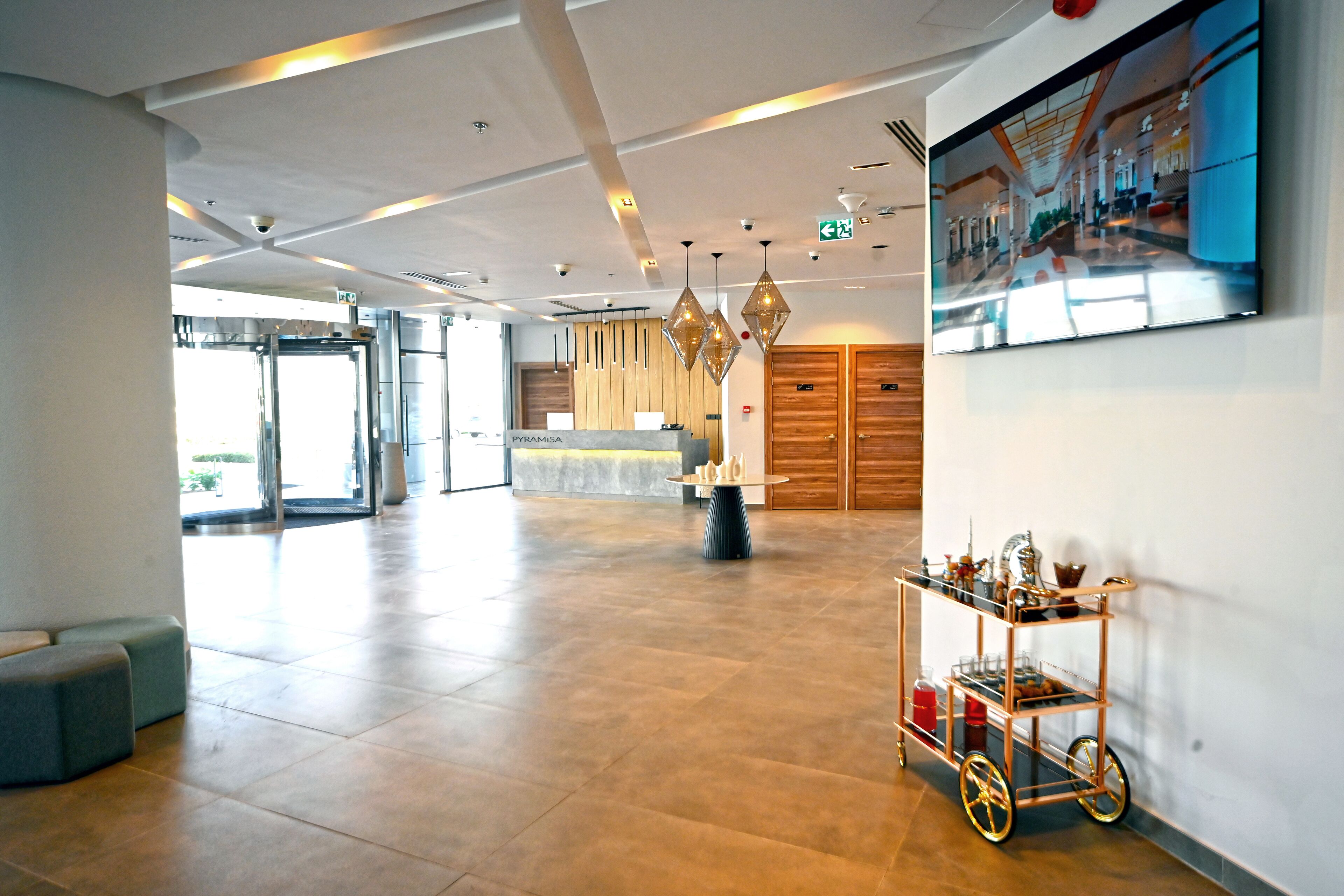 Eine großzügige Lobby mit einer Rezeption, einem Kaffeeangebot und einem großen, an der Wand befestigten Fernseher.