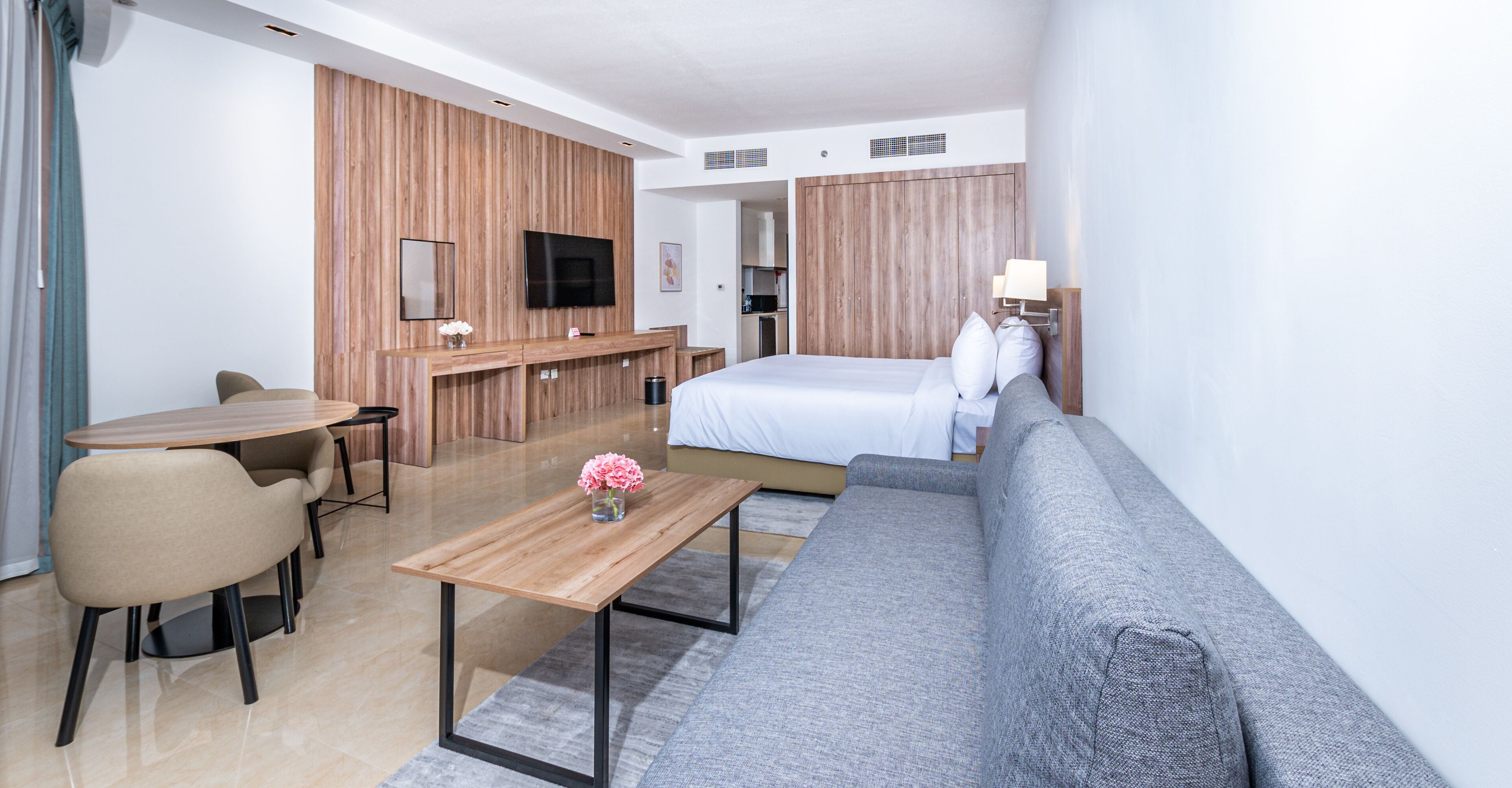 A modern hotel room with a bed, sofa, desk, and TV.