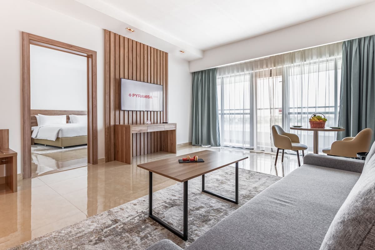 Een moderne hotelkamer met een houten receptiebalie, een flatscreen televisie, een bank, een bijzettafeltje en een zithoek met stoelen en een tafel.