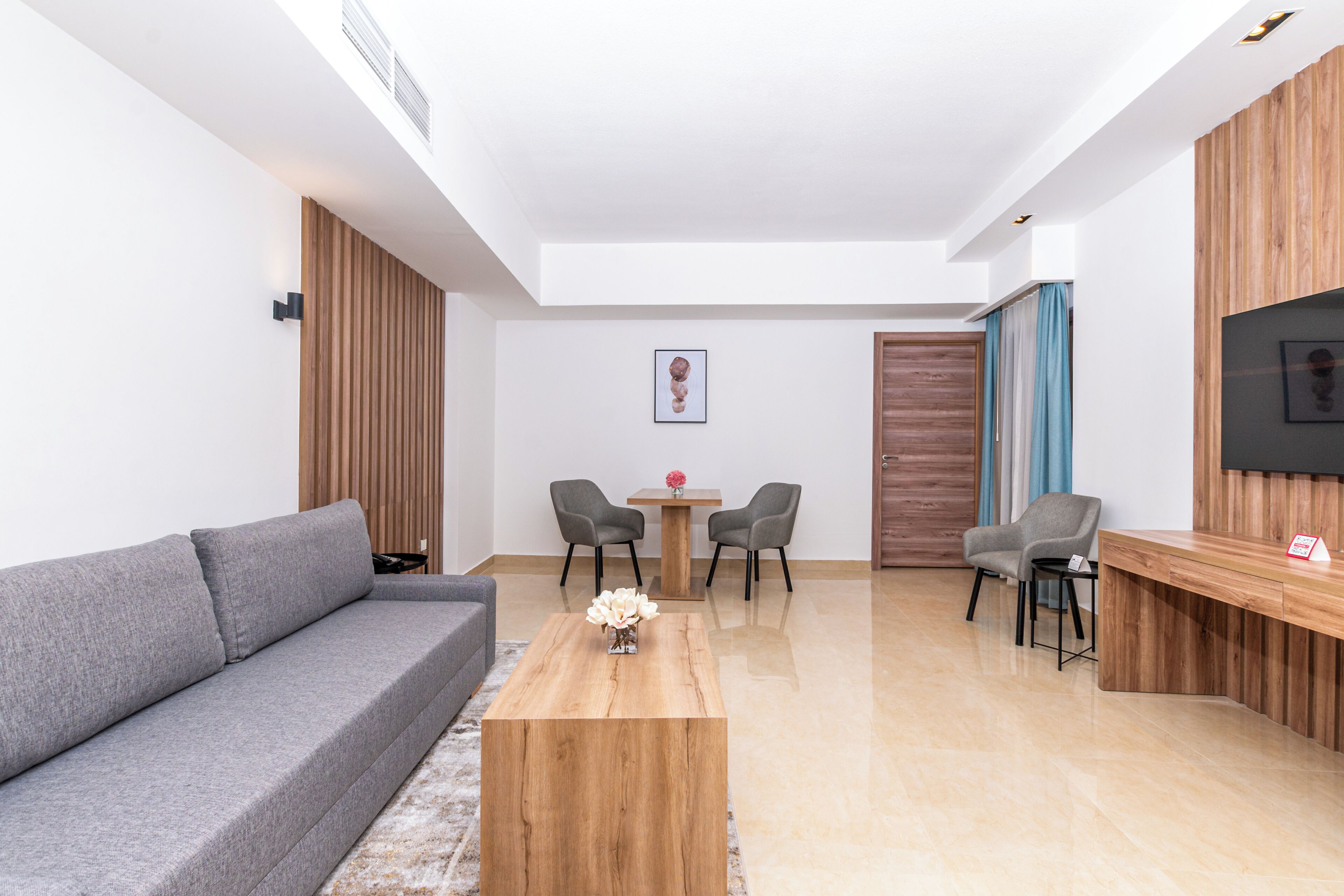 Un salon moderne avec un canapé gris, une table basse en bois et un téléviseur fixé au mur.