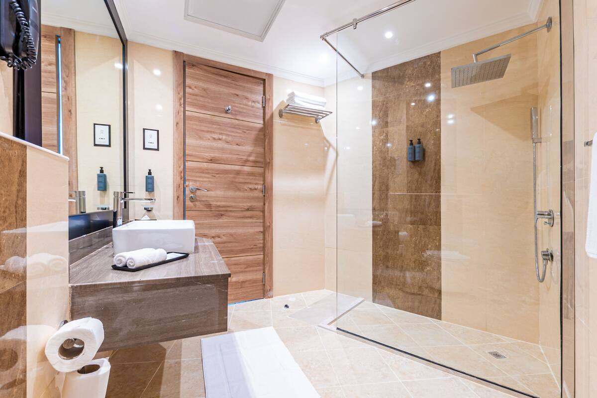 Een moderne badkamer met een houten wastafelmeubel, een douchecabine van glas en een marmeren vloer.