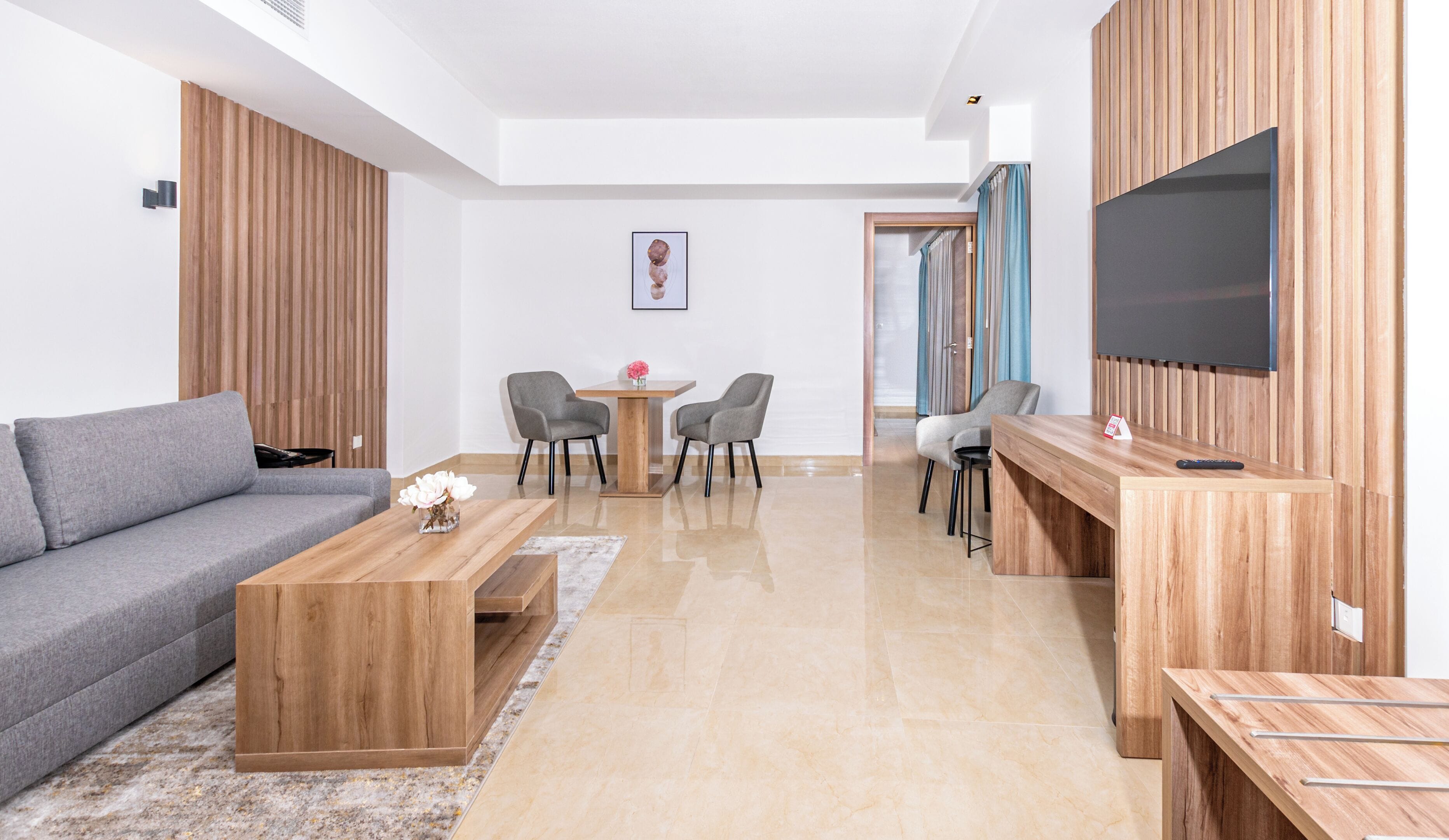 Een moderne woonkamer met een grijze bank, een houten salontafel en een aan de muur bevestigde televisie.