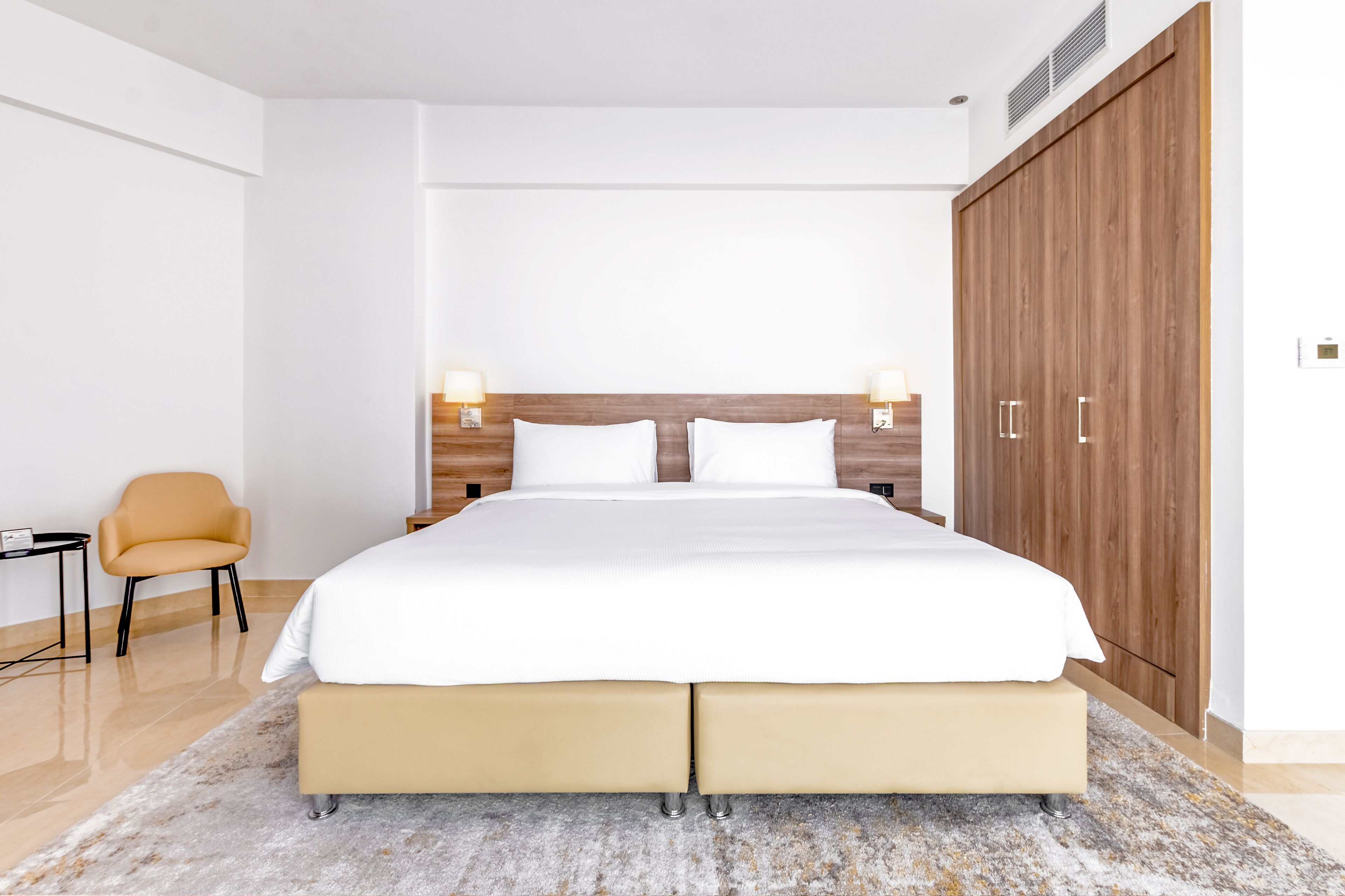 Een moderne slaapkamer met een groot bed, een houten hoofdbord, bedlampjes en een kledingkast.