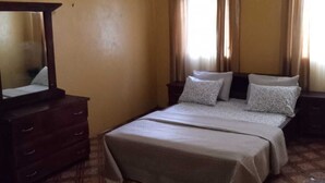 Een slaapkamer met een bed, een dressoir, een plafondventilator en gordijnen.