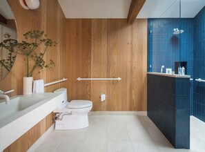 A modern bathroom with a wooden wall, a white toilet, a sink with a mirror, and a shower area with blue tiles.
