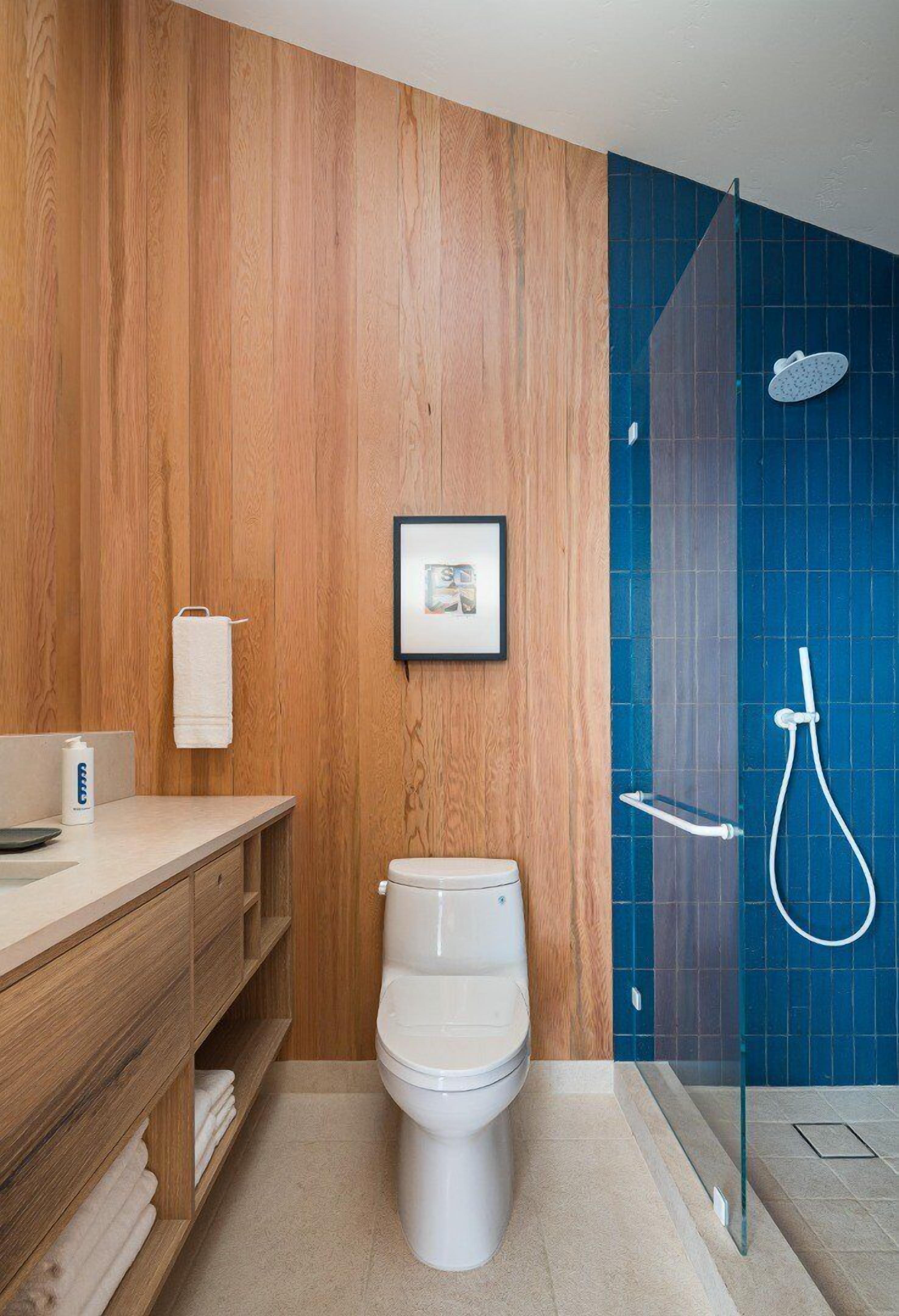 A bathroom with a wooden vanity, a toilet, a framed picture, and a shower area with a glass door.