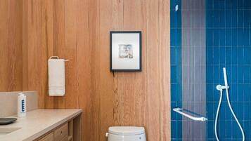 A bathroom with a wooden vanity, a toilet, a framed picture, and a shower area with a glass door.