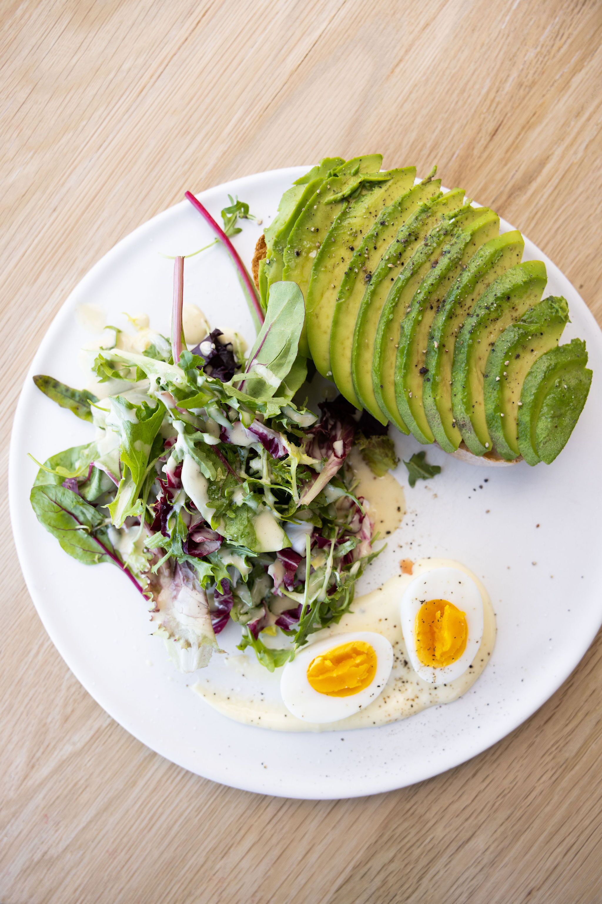 A plate with sliced avocado, a salad, and two halves of a boiled egg.