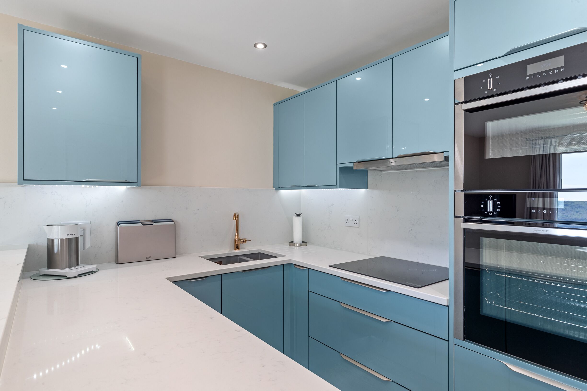 A modern kitchen with teal cabinets, a stainless steel sink, and an oven.