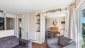 Een moderne woonkamer met een bank, een eethoek met een tafel en stoelen, en een keuken die door een open deur zichtbaar is.