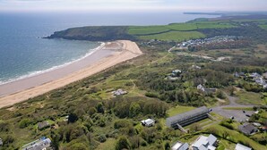 Luchtbeeld van een kustgebied met een strand, woongebouwen en groene velden.
