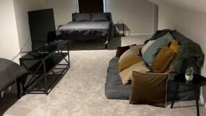 Un pequeño dormitorio en ático, tenuemente iluminado, con una cama individual, un sofá y un mueble para televisión.
