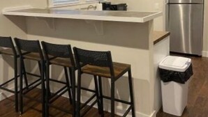 Una cocina con isla blanca, refrigerador de acero inoxidable y tres taburetes de bar.