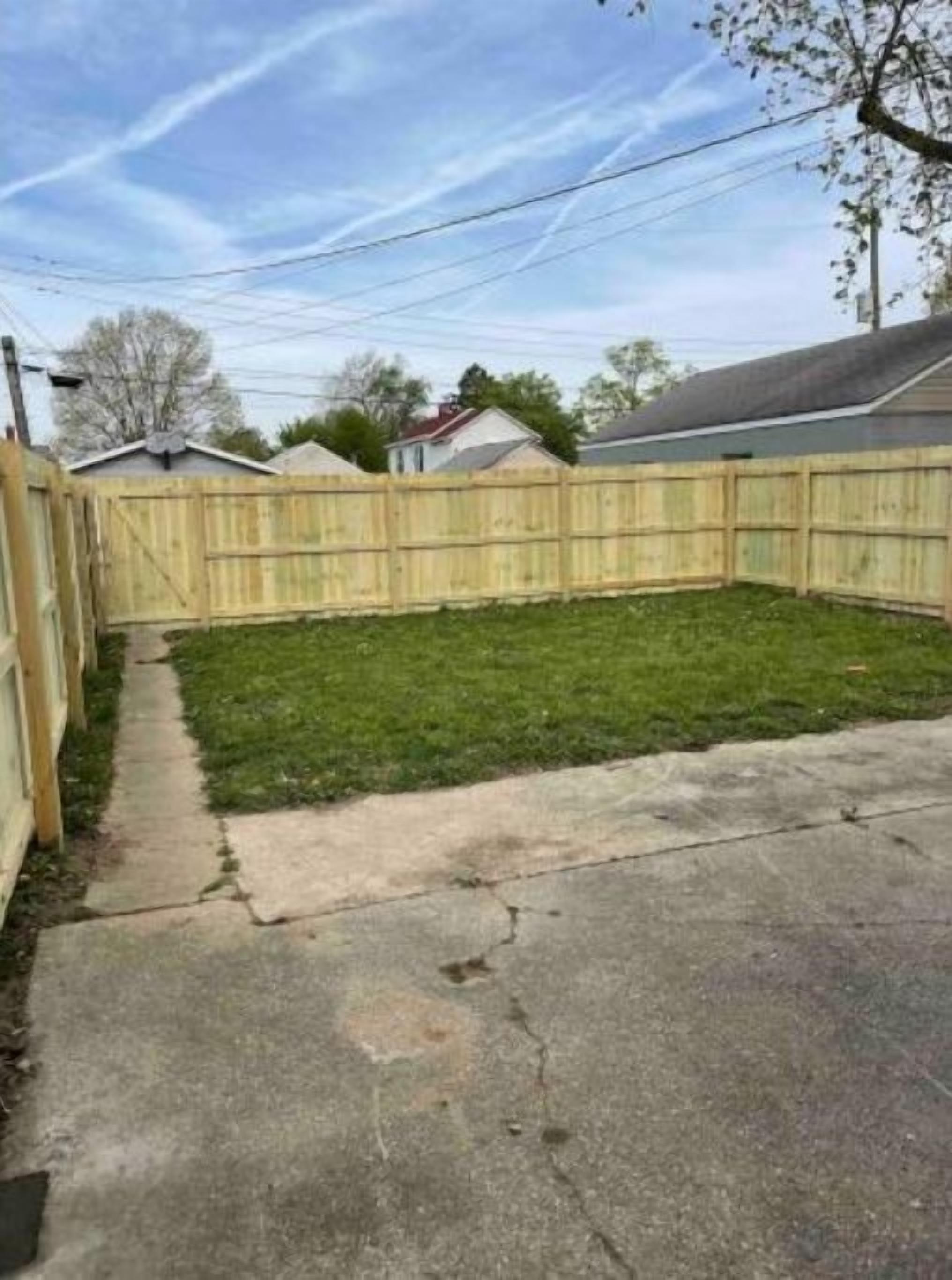 A backyard with a wooden fence, a concrete pathway, and a grassy area.
