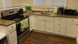 Una cocina con gabinetes blancos, estufa, horno microondas y fregadero.