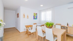 Ein stilvoller Essbereich mit Holztisch und -stühlen, einer Topfpflanze sowie einer Küchenzeile mit Schränken und Arbeitsplatte.