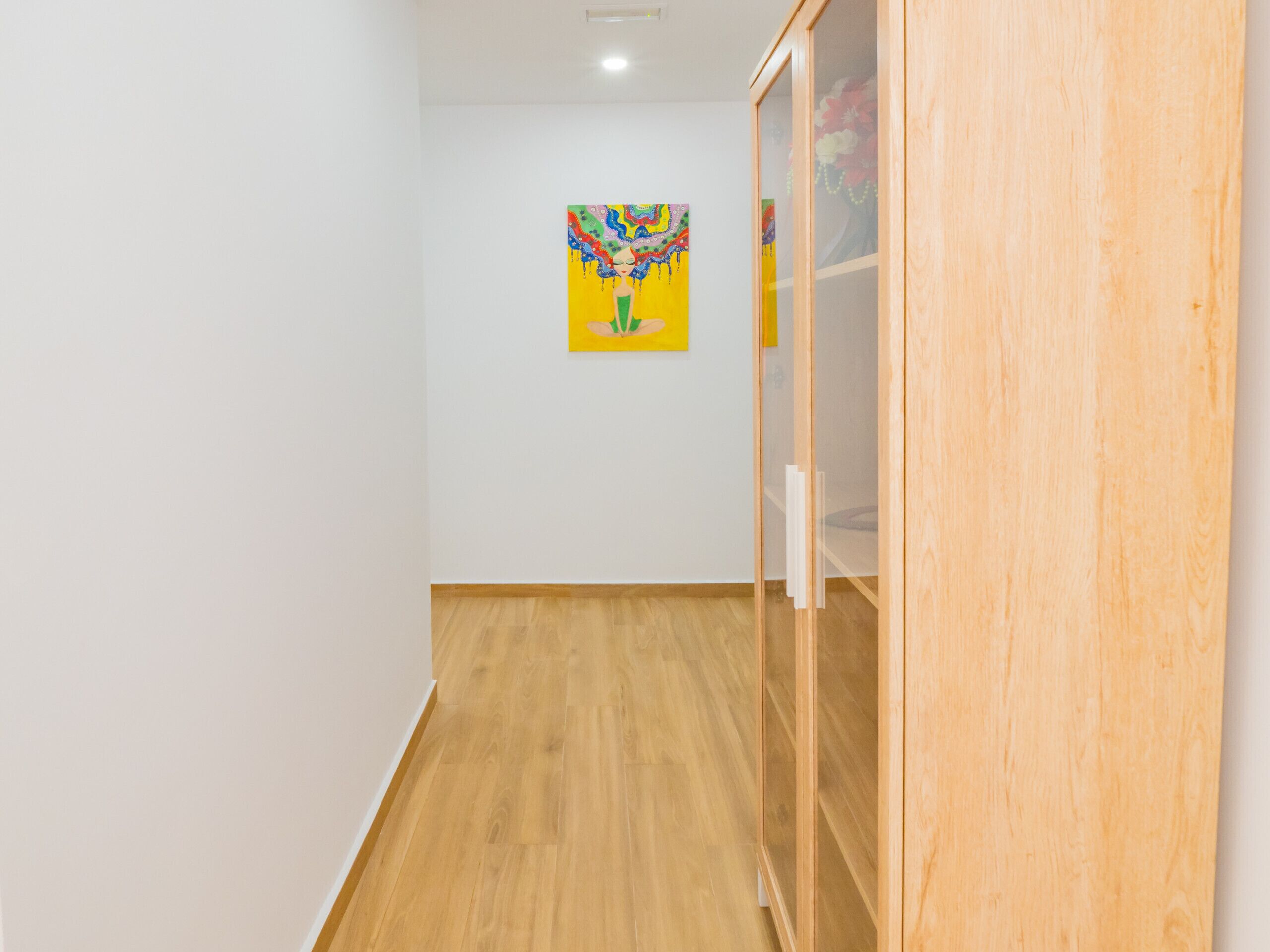 Ein Flur mit Holzdielen, einer weißen Wand und einem farbenfrohen Gemälde an der Wand.