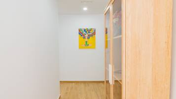Ein Flur mit Holzdielen, einer weißen Wand und einem farbenfrohen Gemälde an der Wand.