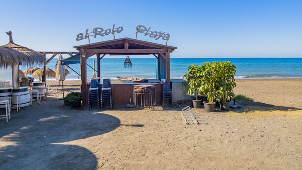 Eine Strandbar namens "Al Roto Playa" mit Außenbereich und einer Struktur mit Reetdach.
