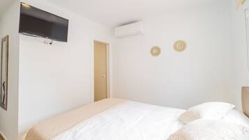 A bedroom with a bed, a mounted TV, an air conditioning unit, and two wall-mounted decorative lights.