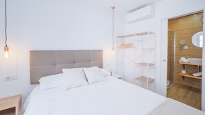 Une chambre à coucher moderne avec un grand lit, une armoire et une salle de bain visible à travers une porte ouverte.