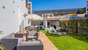 Une terrasse dotée de meubles en osier, d’un espace salon couvert et d’une petite cuisine extérieure.