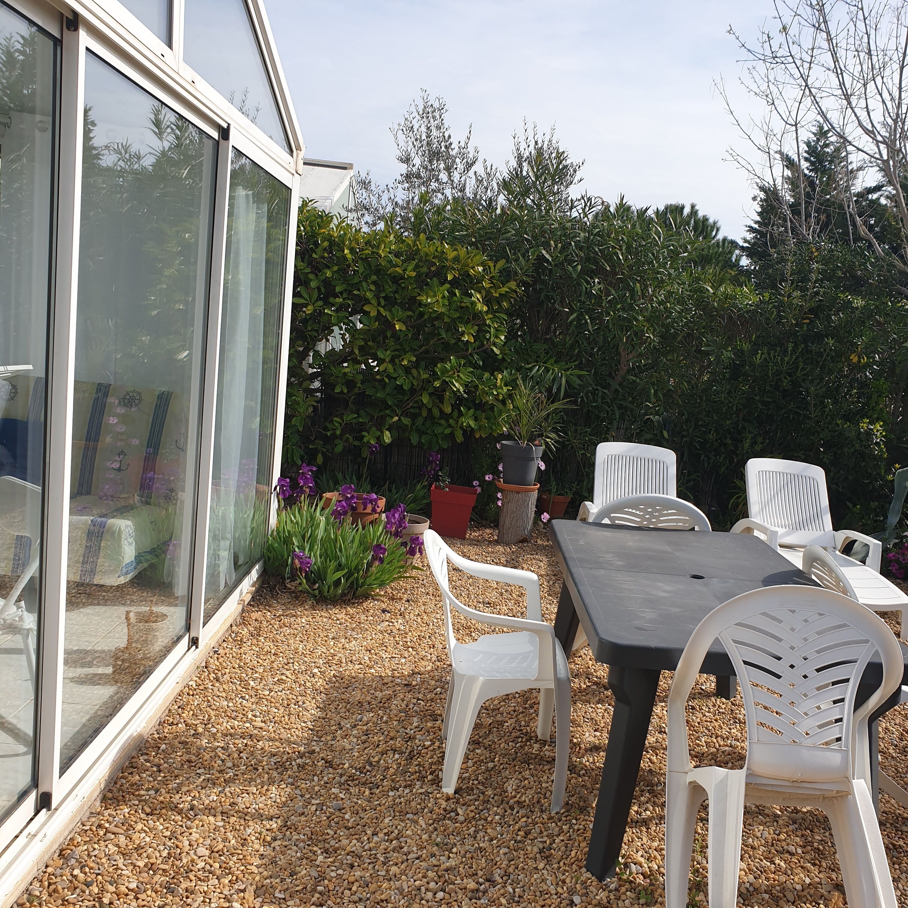 An outdoor patio area with a table and chairs, surrounded by potted plants and a gravel ground.