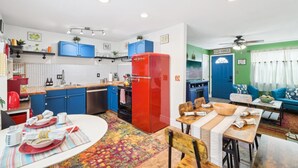 Eine kleine Küche mit blauen Schränken, einem roten Kühlschrank und einem Essbereich mit einem farbenfrohen Teppich.