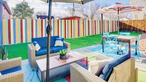 Ein Patio mit Korbmöbeln, einem gestreiften Sonnenschirm und einem farbenfrohen Zaun.