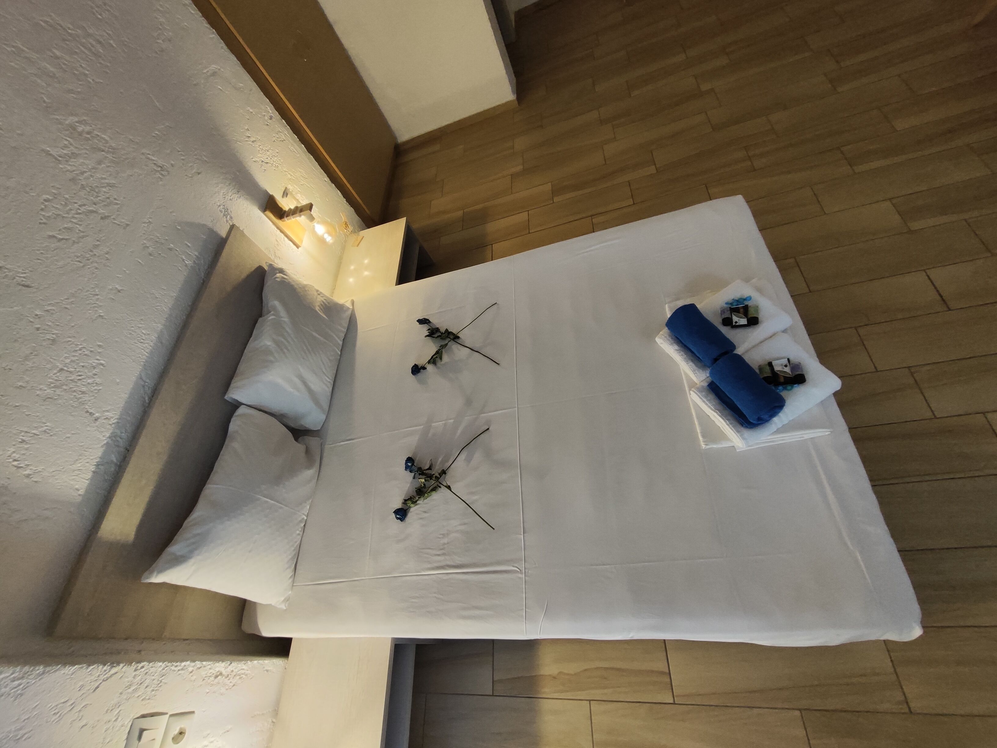 A neatly made bed with white linens, a pillow, and two blue flowers.