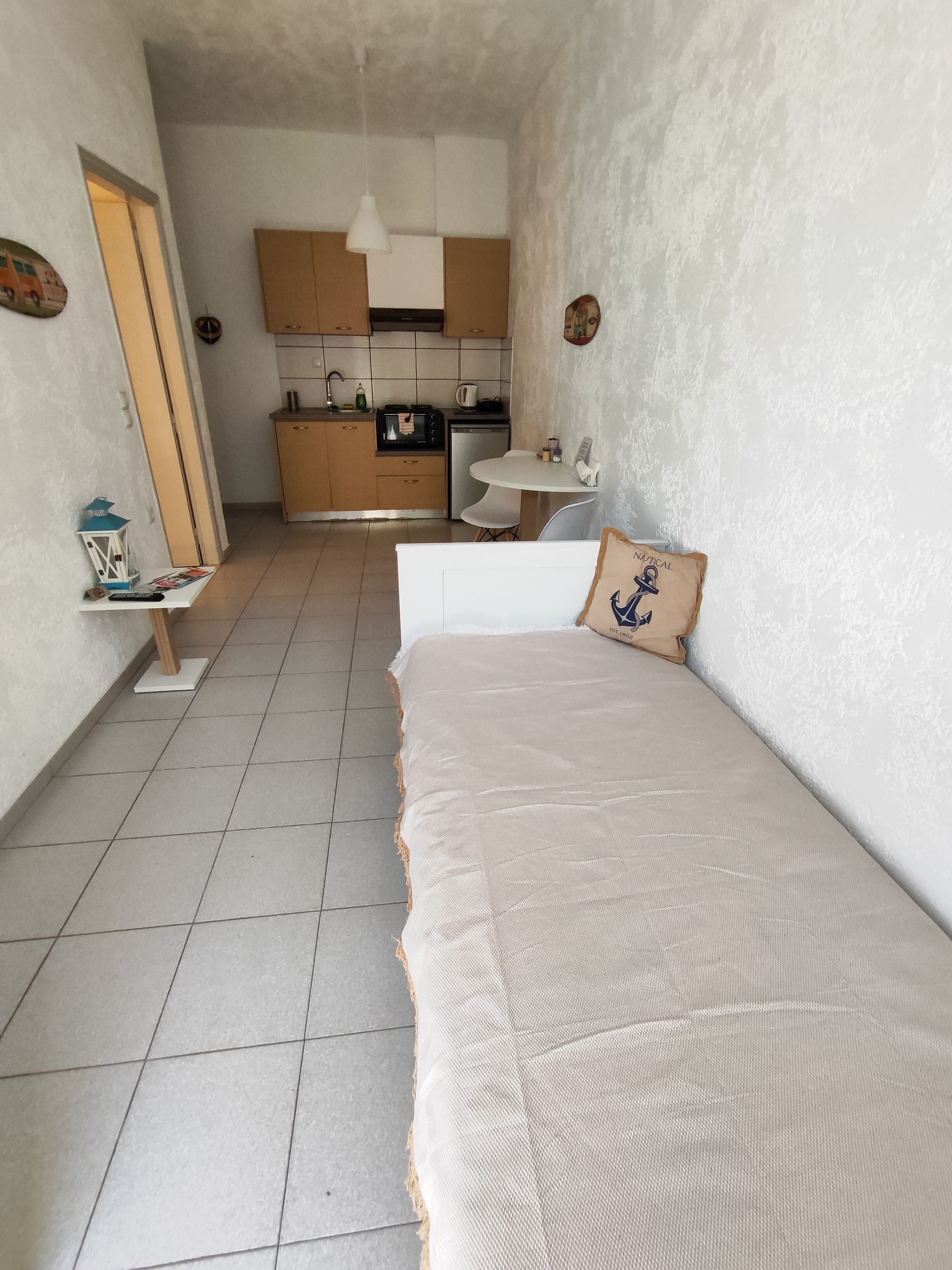 Een compacte hotelkamer met een bed, een klein nachtkastje, een stoel, een kitchenette en een badkamer.