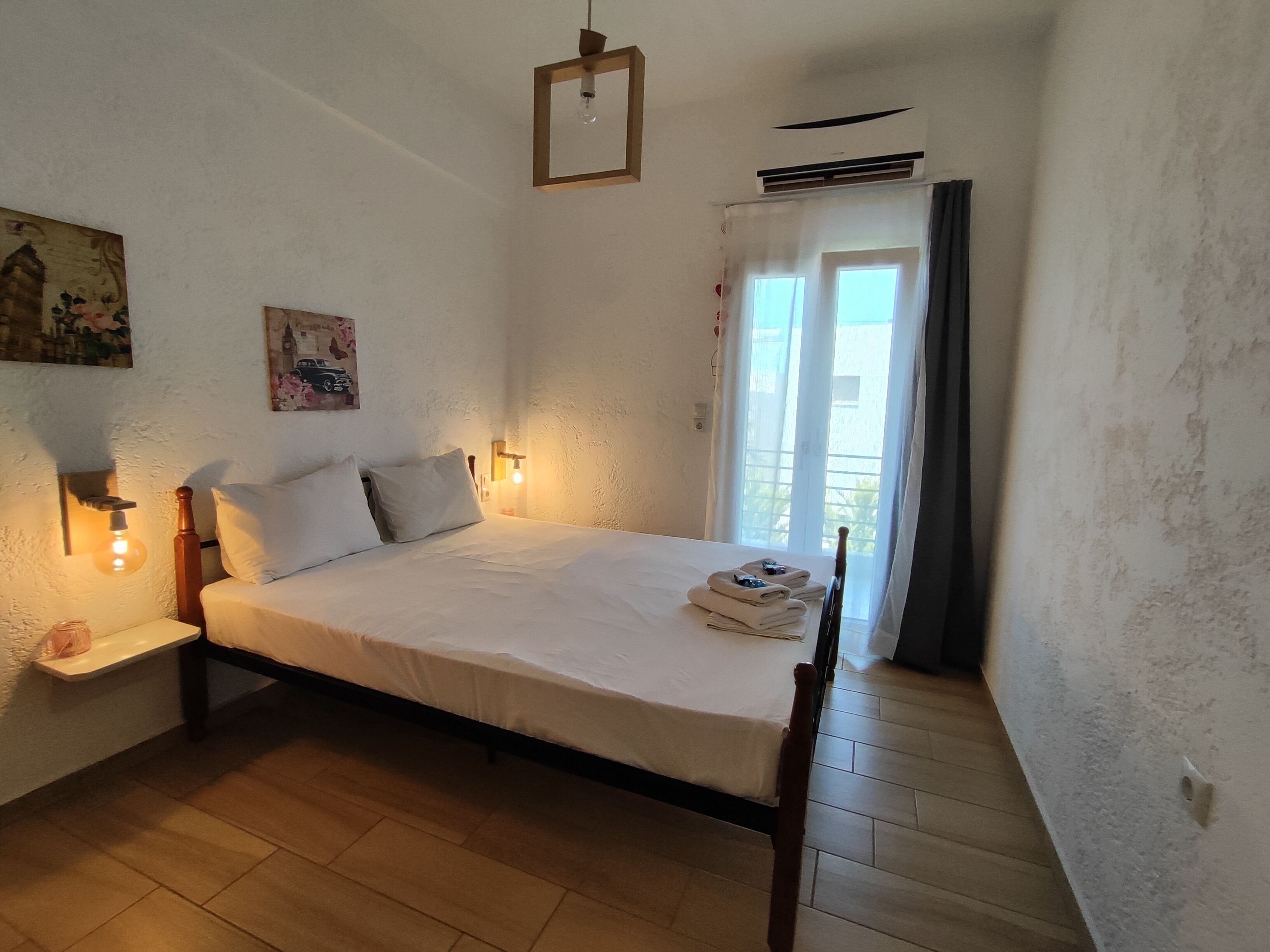 Een slaapkamer met een houten bed, witte lakens, een bedlampje en een raam met gordijnen.