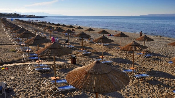 A beach with rows of sun umbrellas and lounge chairs, a clear sky, and a calm sea. - Ble Island (Hersonissos)